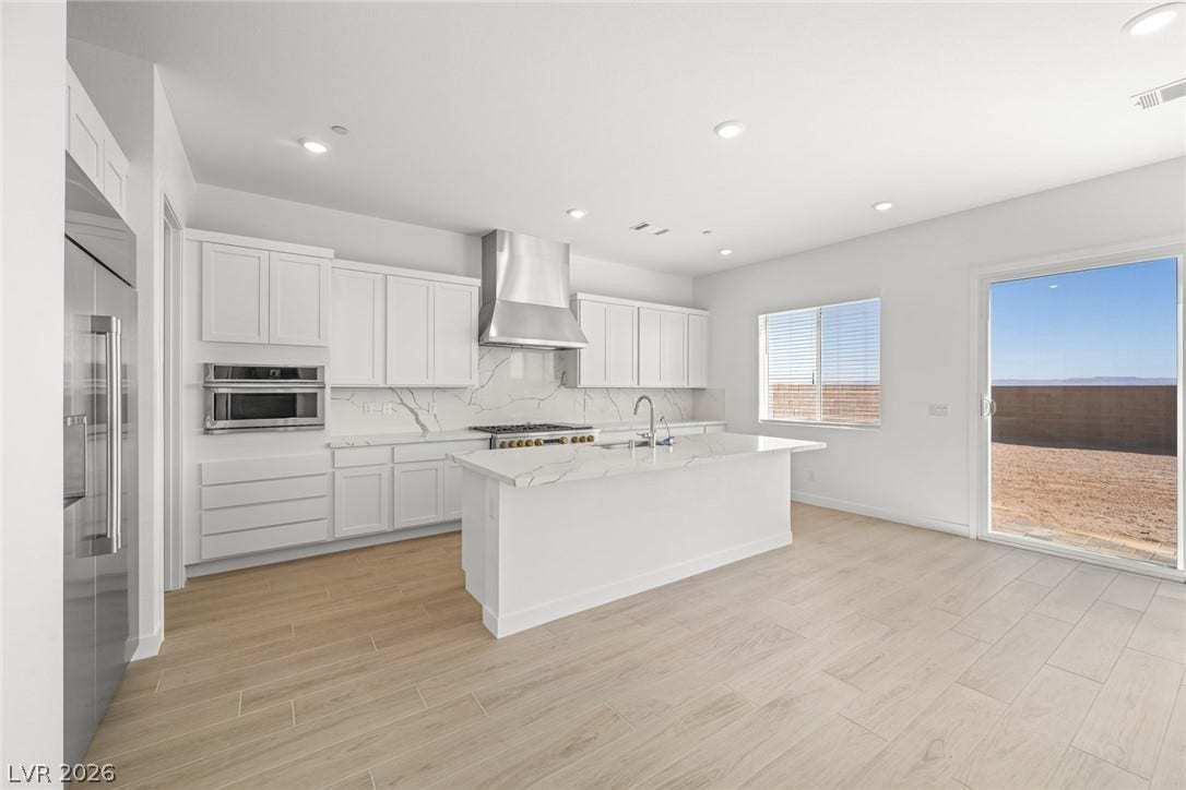 A well-lit kitchen with sleek white cabinetry and a spacious island, opening to an arid outdoor area.