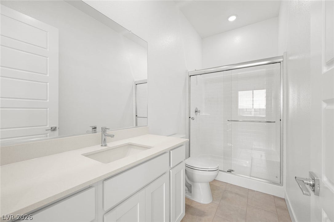 A well-appointed bathroom features a single vanity with stone counters and a spacious, modern glass-enclosed shower.