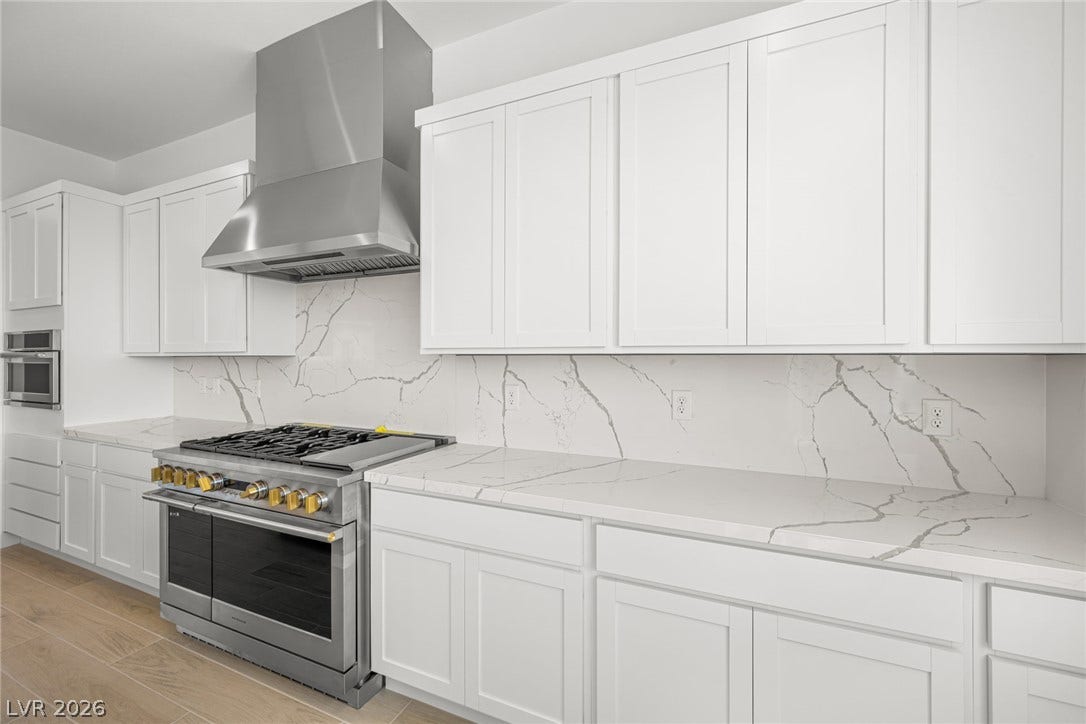 A well-lit culinary space showcases a premium gas range, stainless steel appliances, and white marble countertops.
