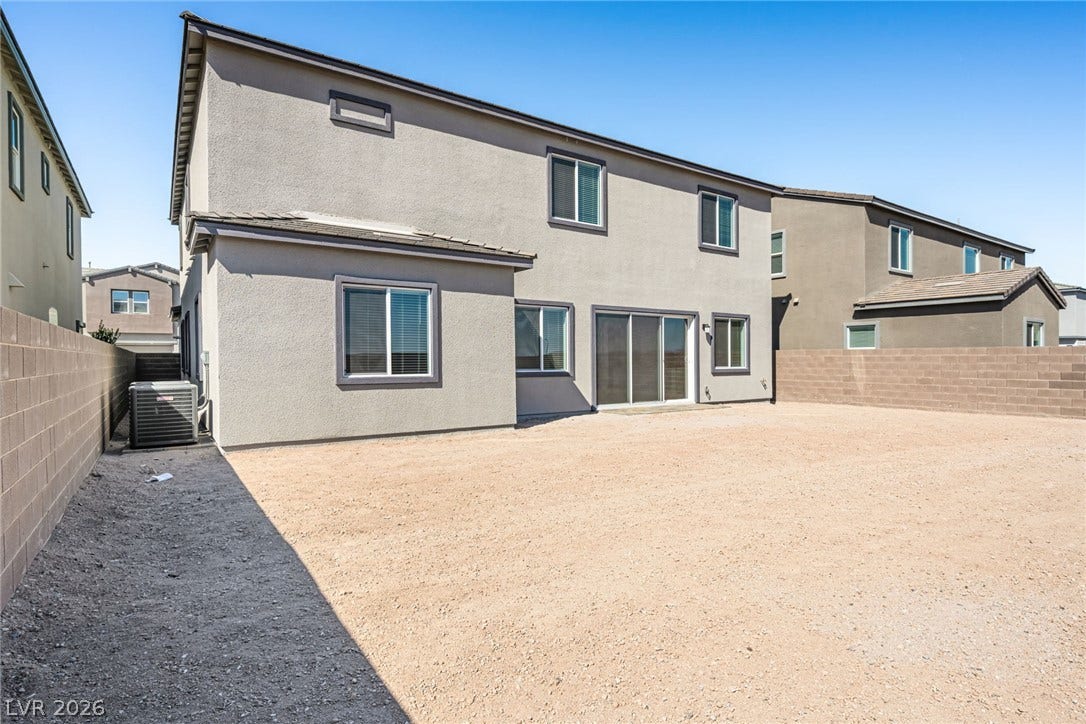 An arid backyard awaits creative landscaping, featuring a stucco exterior with multiple windows and sliding glass doors.