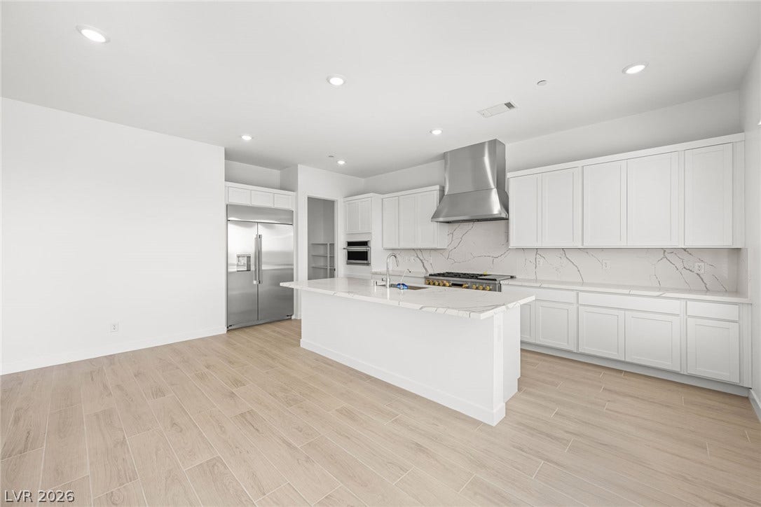 An open-concept kitchen features sleek white cabinetry and marble-patterned countertops, centered around a practical kitchen island.