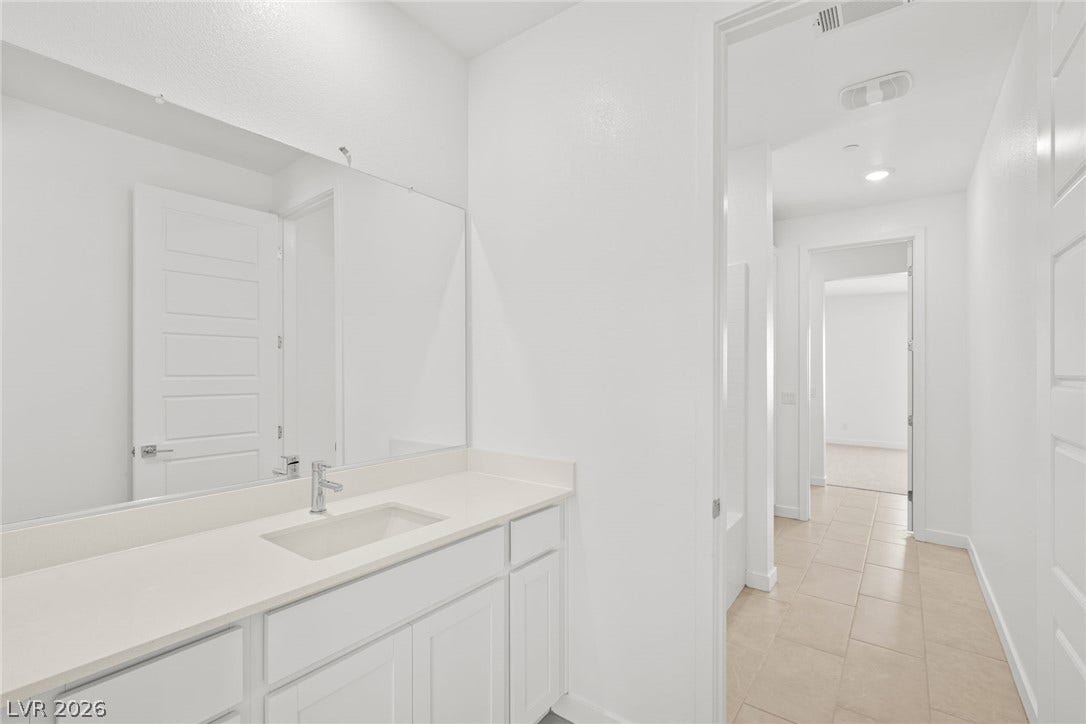 Modern bath vanity and well-lit hallway with tiled flooring.