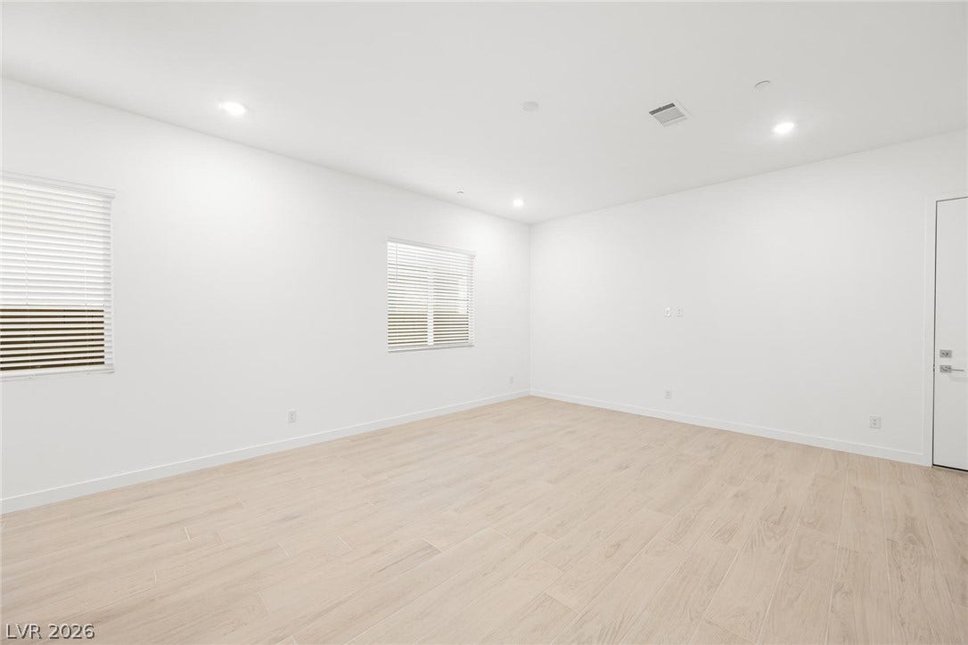 Well-lit living area features pale wood flooring and crisp white walls.