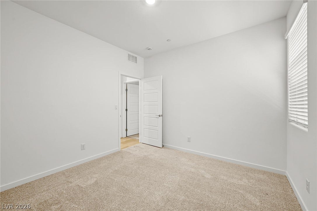 1663 Capri Falls Court, Henderson, NV 89011 A spacious bedroom features soft carpeting, neutral walls, and a large window inviting natural light.