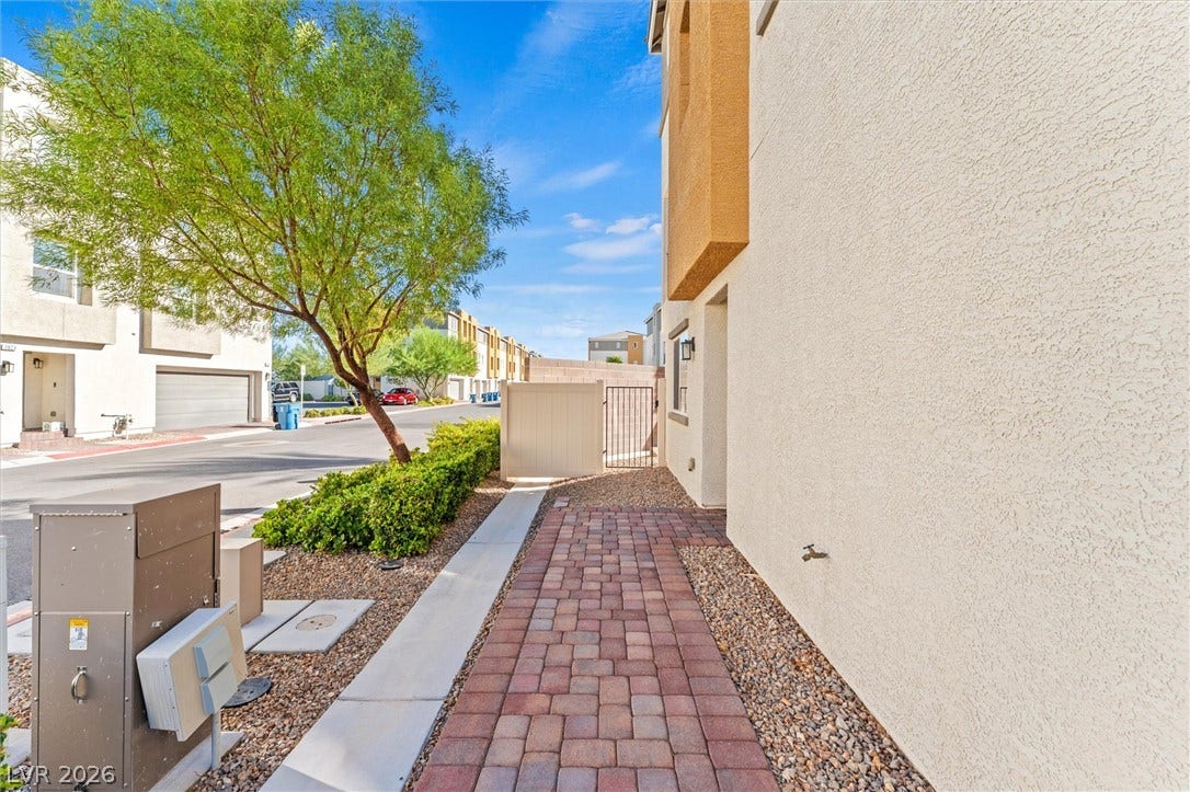 10059 Dazzling Sunrays Avenue, Las Vegas, NV 89129 A paved brick walkway leads along the stucco exterior toward a gated side yard entry.