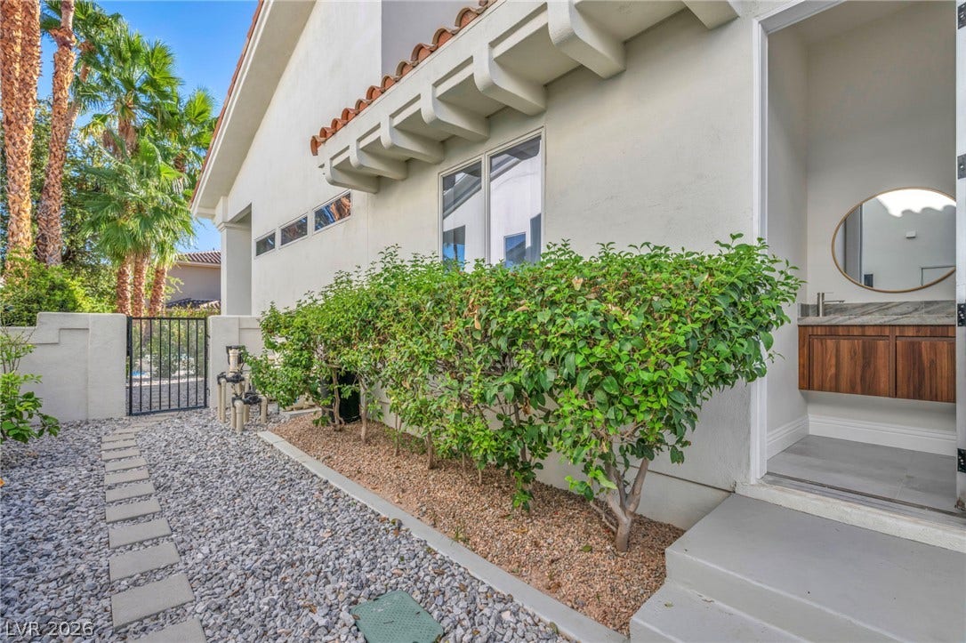 8805 Spanish Mountain Drive, Las Vegas, NV 89148 Gravel pathways wind past manicured hedges toward a modern stucco exterior with direct bathroom access.