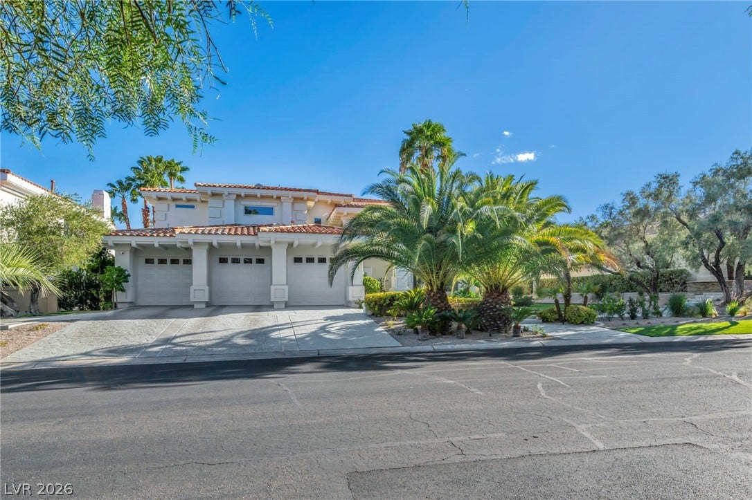 8805 Spanish Mountain Drive, Las Vegas, NV 89148 Mature palms frame a three-car garage and classic tile roof under a clear blue sky.