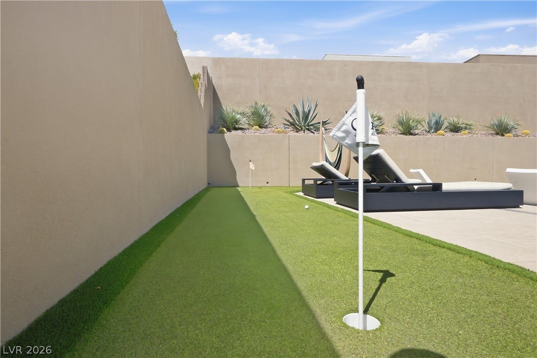 High privacy walls frame a manicured putting green alongside a paved patio area.