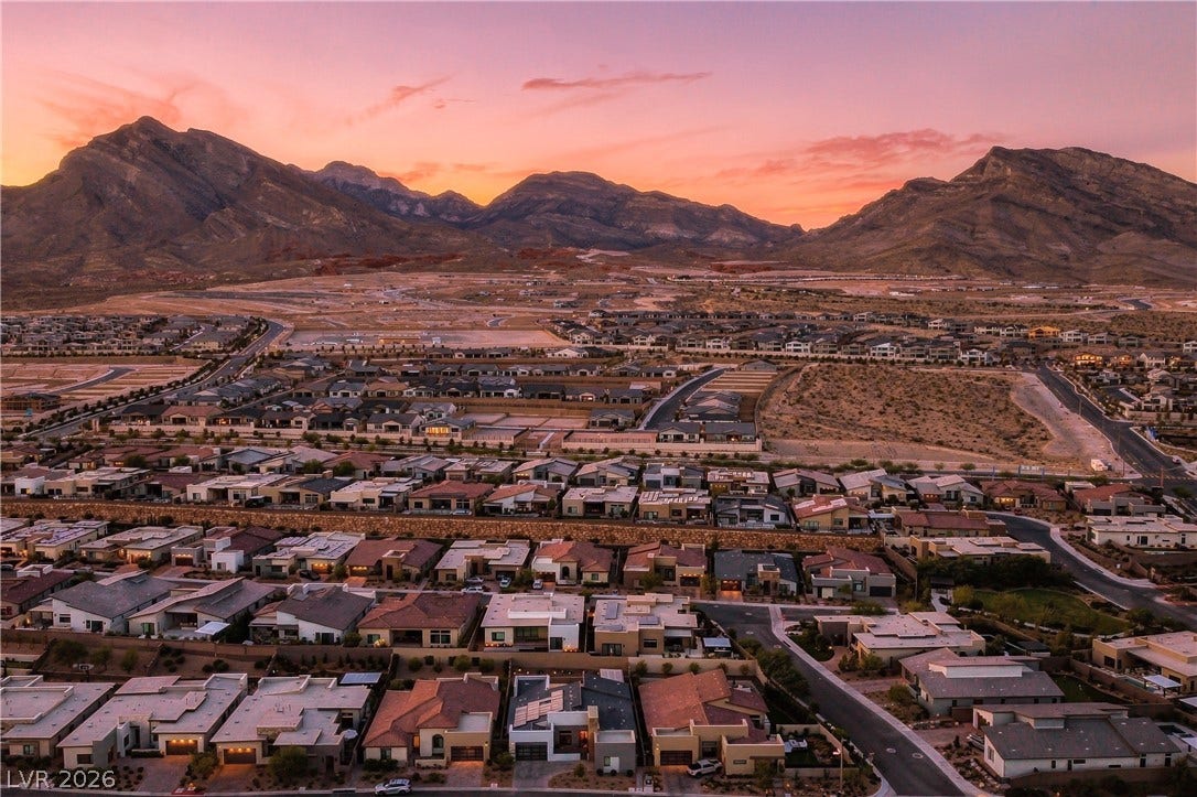 Dramatic mountain peaks frame a sprawling valley neighborhood under a vibrant sunset sky.