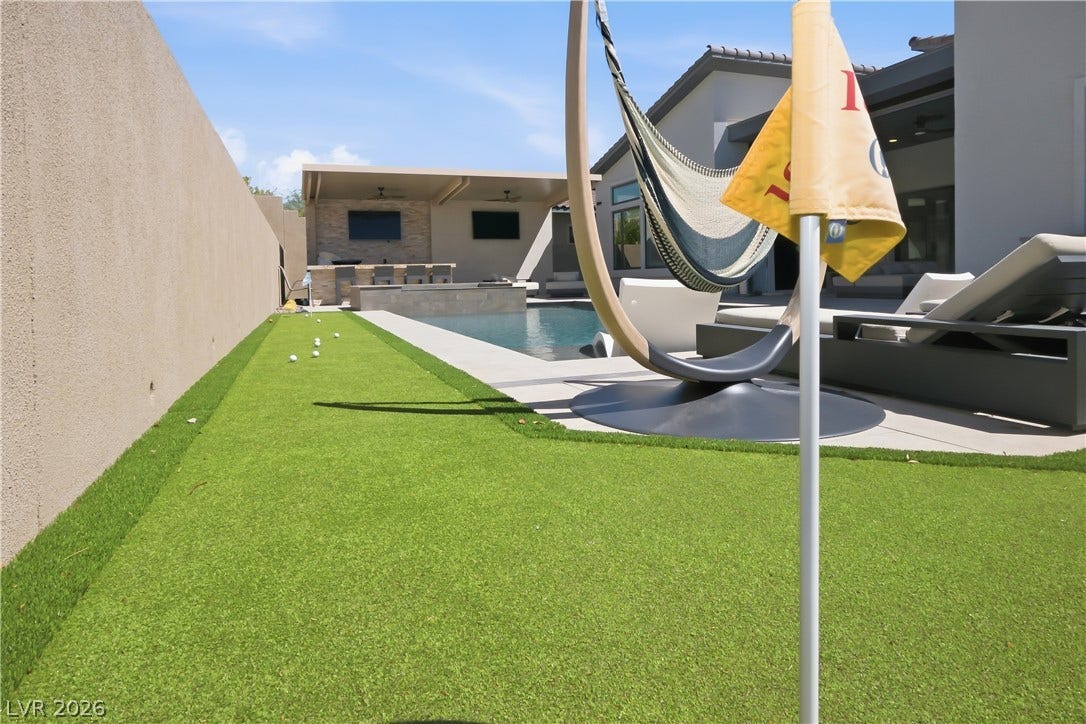 An inviting backyard oasis features a putting green alongside a pristine swimming pool.