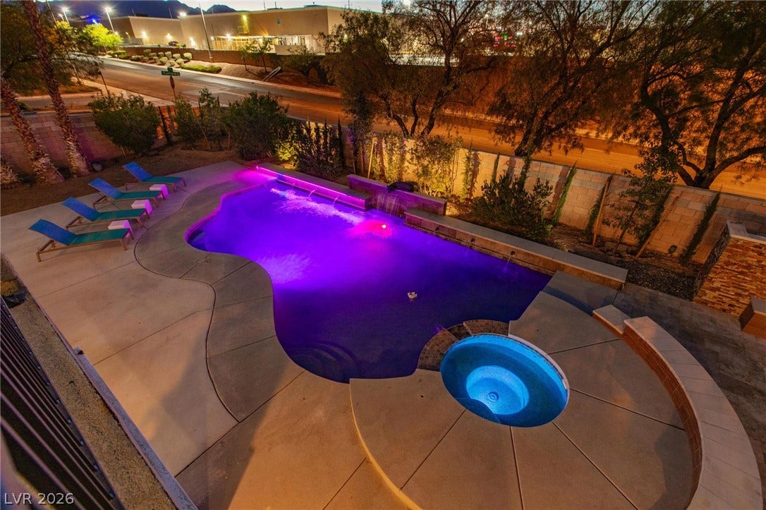 8088 Dark Hollow Place, Las Vegas, NV 89117 A private backyard oasis features an illuminated swimming pool with a connected spa and lounging area.