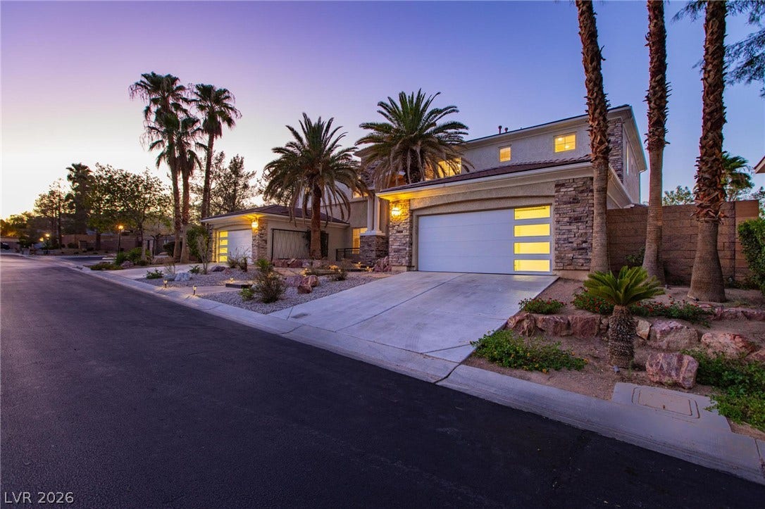 8088 Dark Hollow Place, Las Vegas, NV 89117 Illuminated garages and tropical landscaping frame this striking residence at dusk.