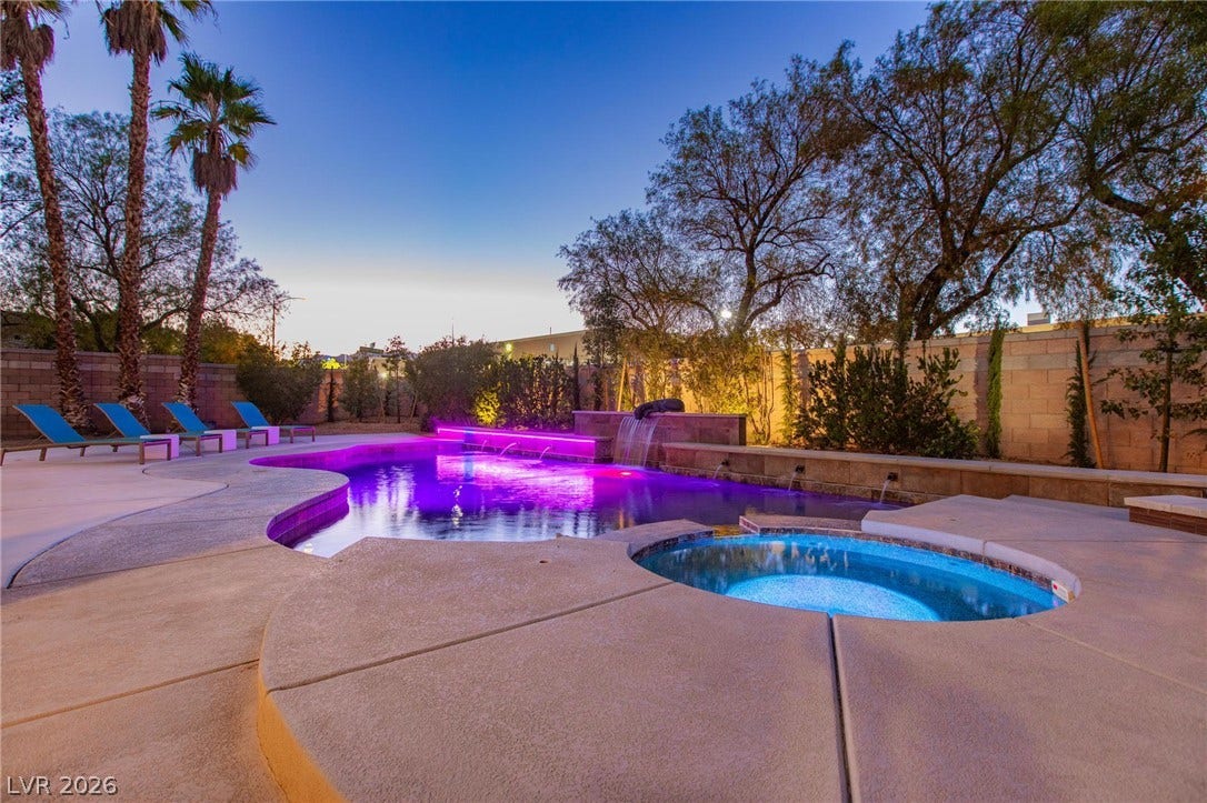 8088 Dark Hollow Place, Las Vegas, NV 89117 An illuminated backyard oasis featuring a custom-shaped pool and integrated spa, surrounded by concrete decking and mature landscaping.