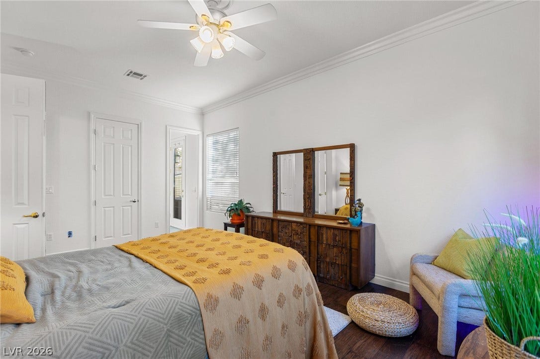 8088 Dark Hollow Place, Las Vegas, NV 89117 A well-lit bedroom features hardwood flooring and crown molding, enhanced by natural light from a window and a modern ceiling fan.