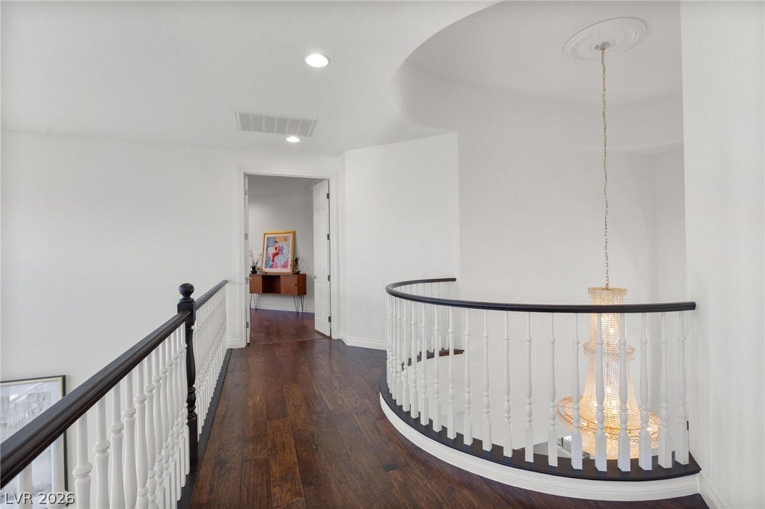 8088 Dark Hollow Place, Las Vegas, NV 89117 Elegant hardwood flooring leads through a well-lit hallway with a classic chandelier and graceful curved staircase.