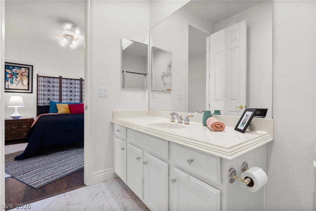 8088 Dark Hollow Place, Las Vegas, NV 89117 White vanity with a large mirror provides ample space in this well-appointed bathroom, conveniently adjacent to a comfortable bedroom.
