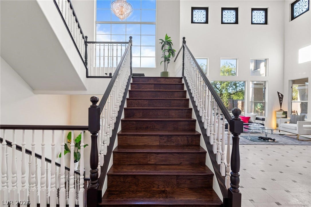 8088 Dark Hollow Place, Las Vegas, NV 89117 A grand wooden staircase with white balusters ascends to an upper level, complementing the bright, open living space below.