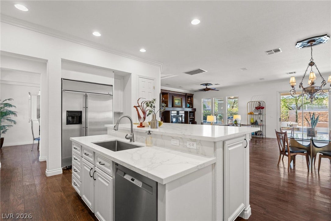 8088 Dark Hollow Place, Las Vegas, NV 89117 An inviting open-concept kitchen boasts a large island with white stone counters and a stainless steel sink, flowing into a spacious living area.