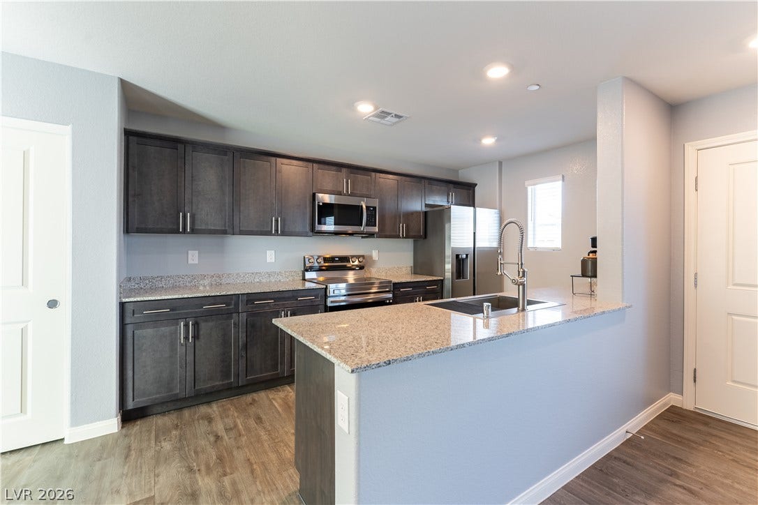 6911 Orange Horizon Street, North Las Vegas, NV 89086 Rich dark cabinetry and sleek stone countertops define this modern, open culinary space.