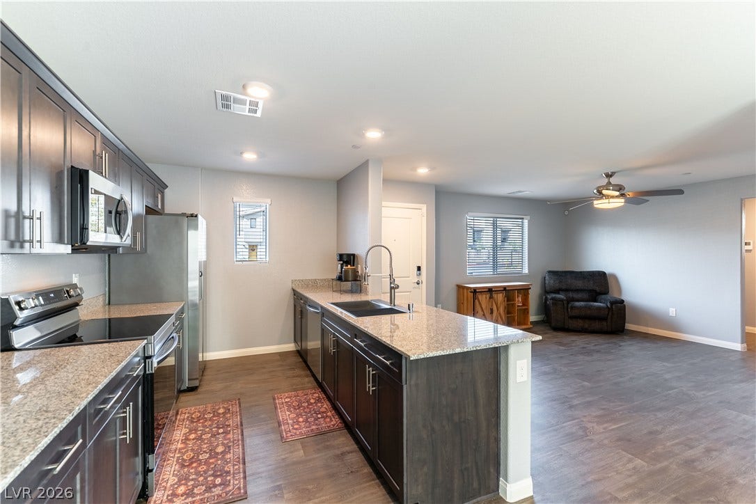 6911 Orange Horizon Street, North Las Vegas, NV 89086 Gleaming stone countertops and dark cabinetry anchor this airy, open-concept living and cooking space.