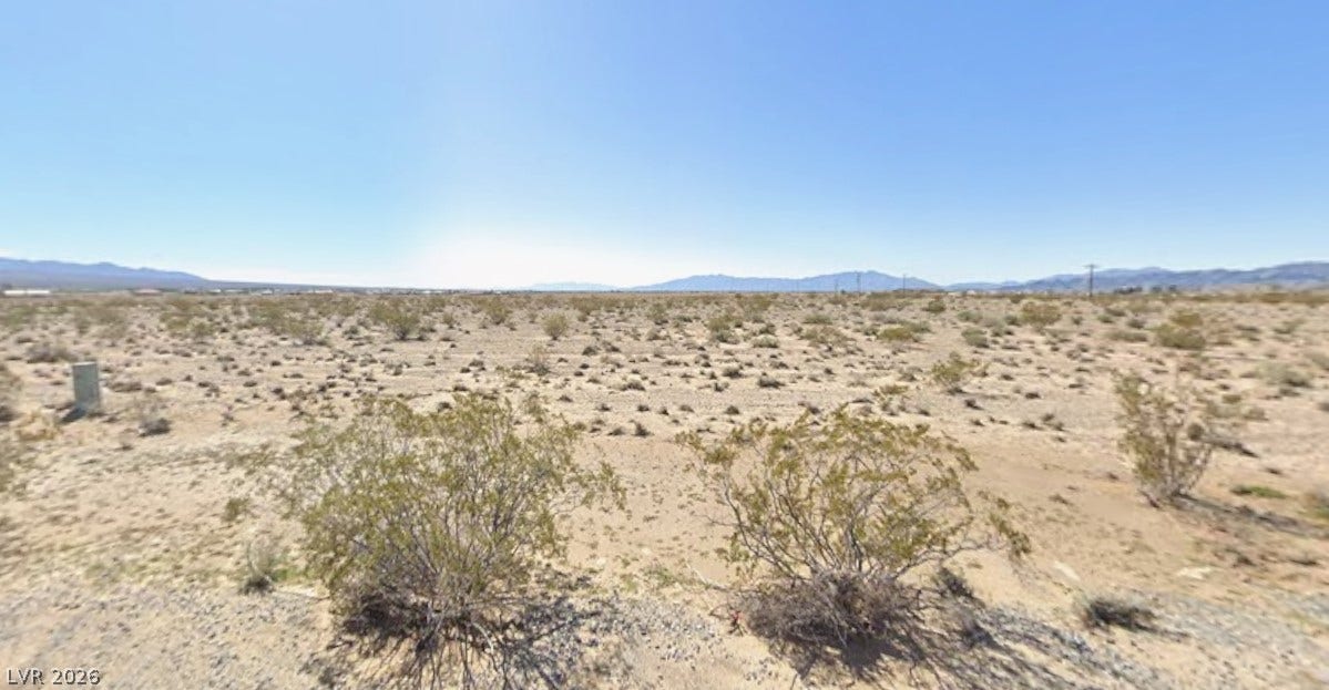 Vast desert sands stretch toward distant mountain ranges under a clear blue sky.