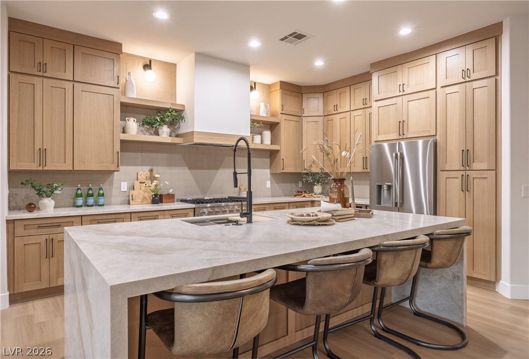 10248 Andante Court, Las Vegas, NV 89135 Kitchen with light wood-type flooring, light stone counters, an island with sink, stainless steel refrigerator with ice dispenser, and a kitchen breakfast bar