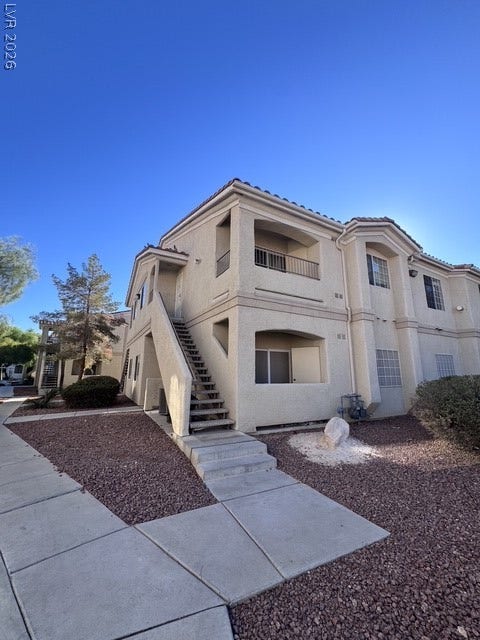 1881 W Alexander Road, #2107, North Las Vegas, NV 89032 A concrete walkway leads past desert landscaping to the entrance of this multi-level stucco building.