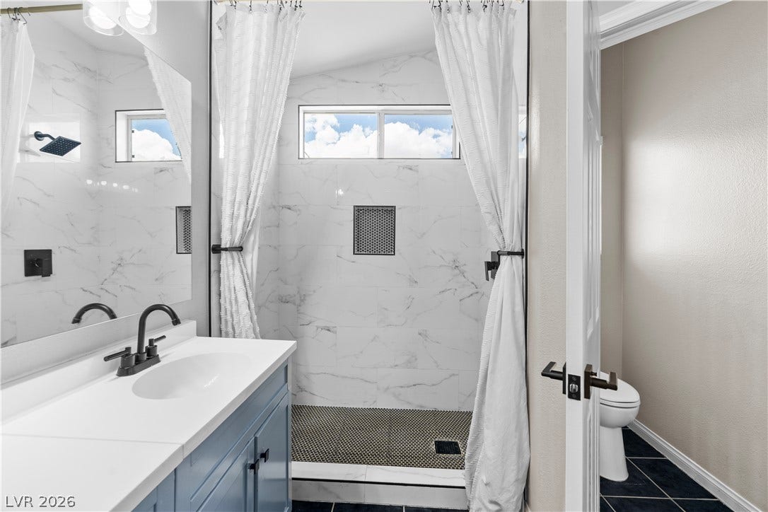 4927 Rancho Domingo Court, North Las Vegas, NV 89031 Gleaming stone tile walls surround a walk-in shower with modern black fixtures.