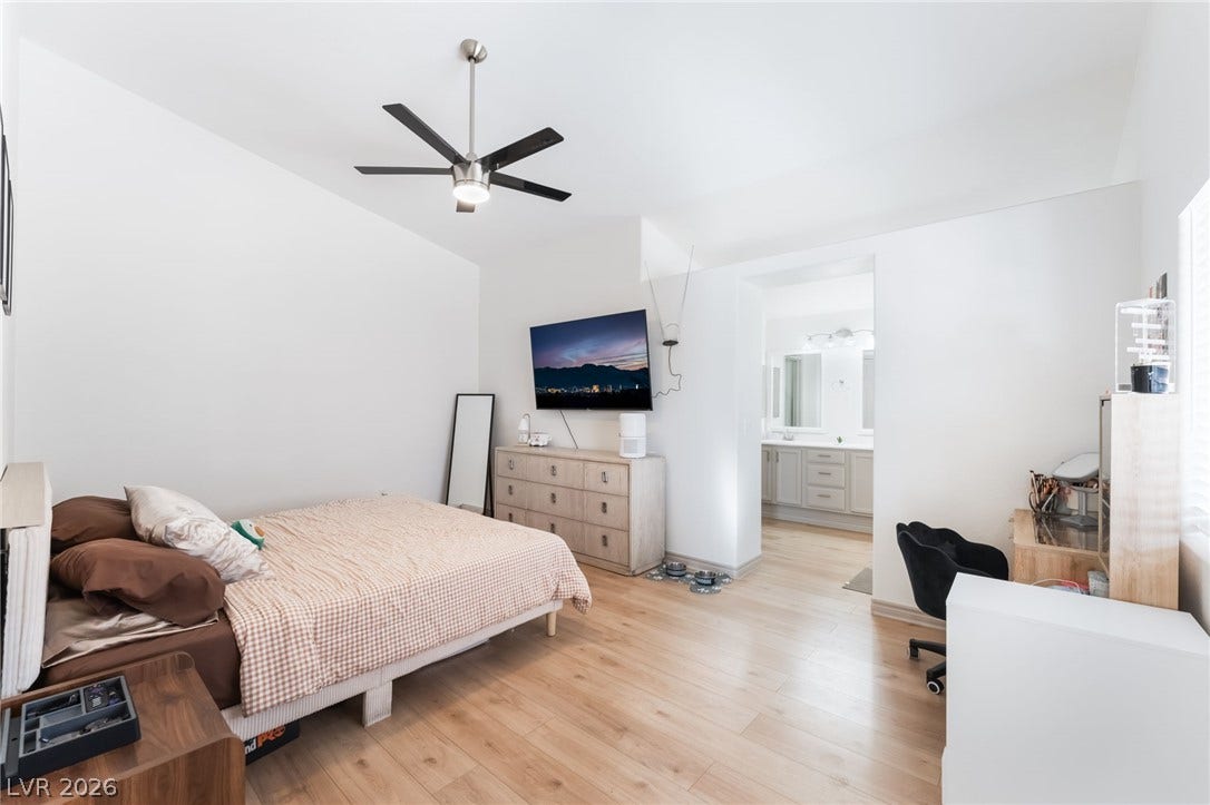 3729 Shimmering Creek Avenue, North Las Vegas, NV 89031 A spacious bedroom features natural wood-style flooring and direct access to an en-suite bathroom.