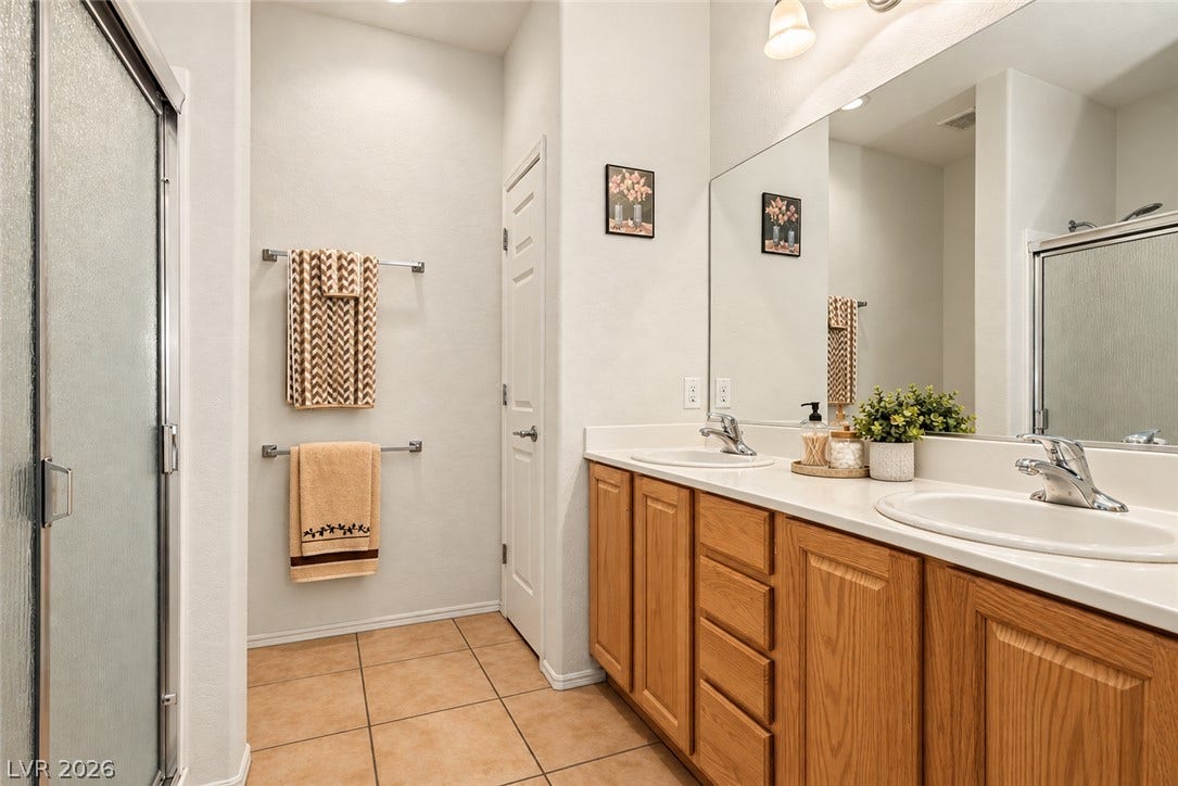 An expansive double vanity sits on warm tile flooring beneath high ceilings.