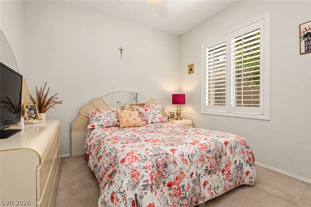 A quiet bedroom offers soft carpeting underfoot alongside a window framed by classic plantation shutters.