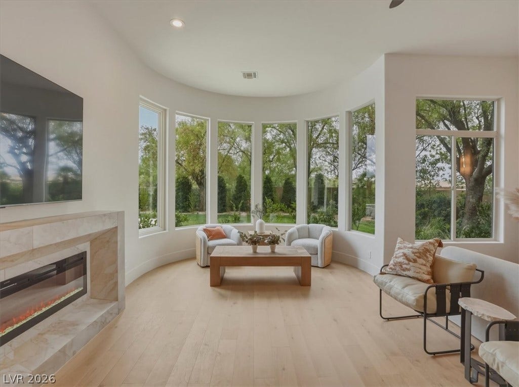 3 Isleworth Drive, Henderson, NV 89052 A graceful living area features a curved wall of windows, framing verdant outdoor views alongside a contemporary fireplace.