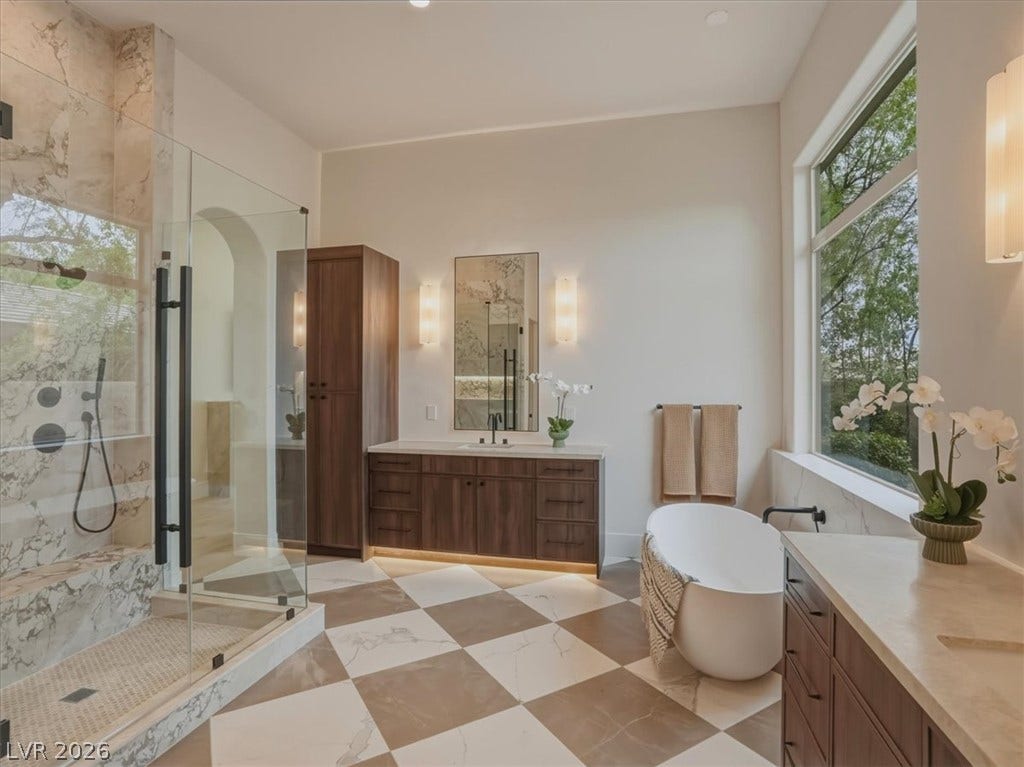 3 Isleworth Drive, Henderson, NV 89052 Luxurious primary bath with a spacious shower, freestanding tub, and dual vanities, all beneath soaring windows.