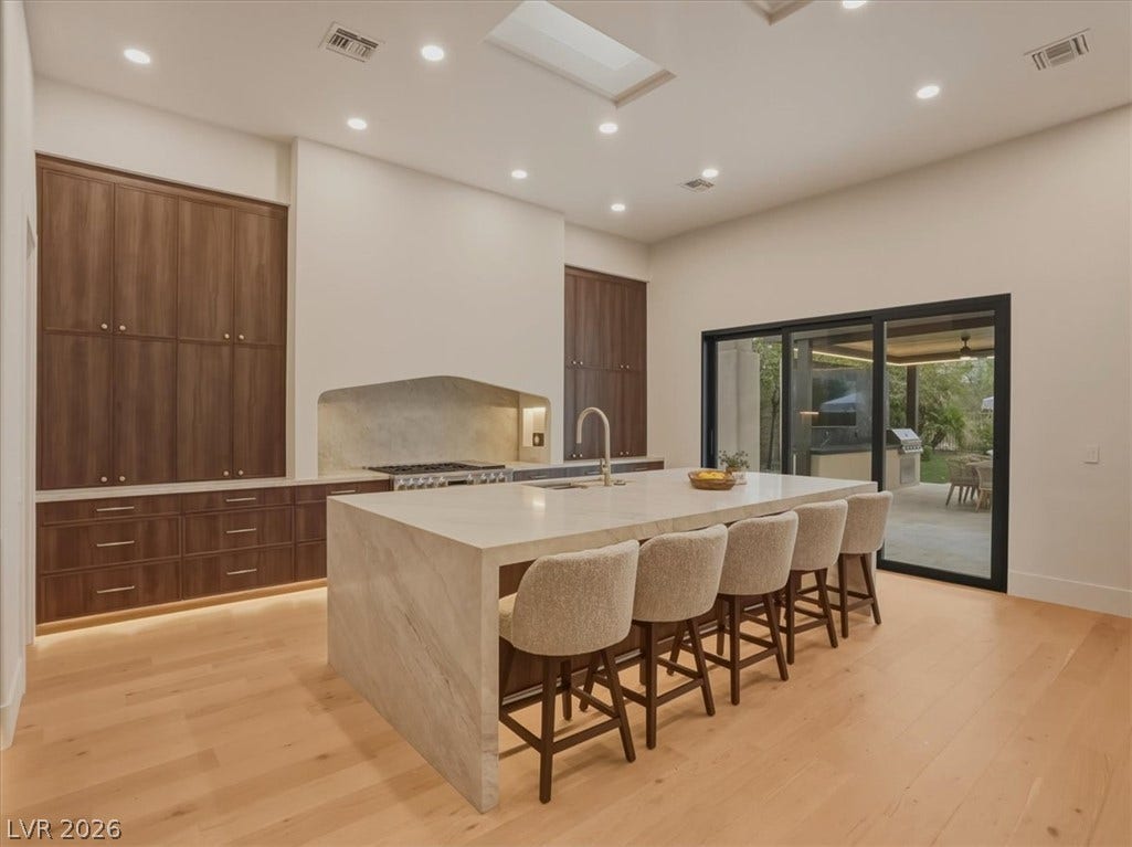3 Isleworth Drive, Henderson, NV 89052 An inviting kitchen features a grand island with seating for six, alongside rich wood cabinetry and light wood flooring.