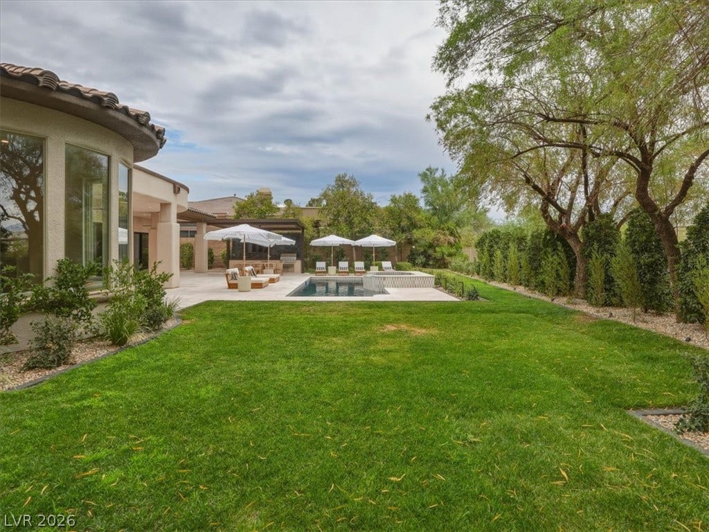 3 Isleworth Drive, Henderson, NV 89052 An inviting backyard oasis features a shimmering pool, ample lounging space, and a manicured lawn framed by mature trees.