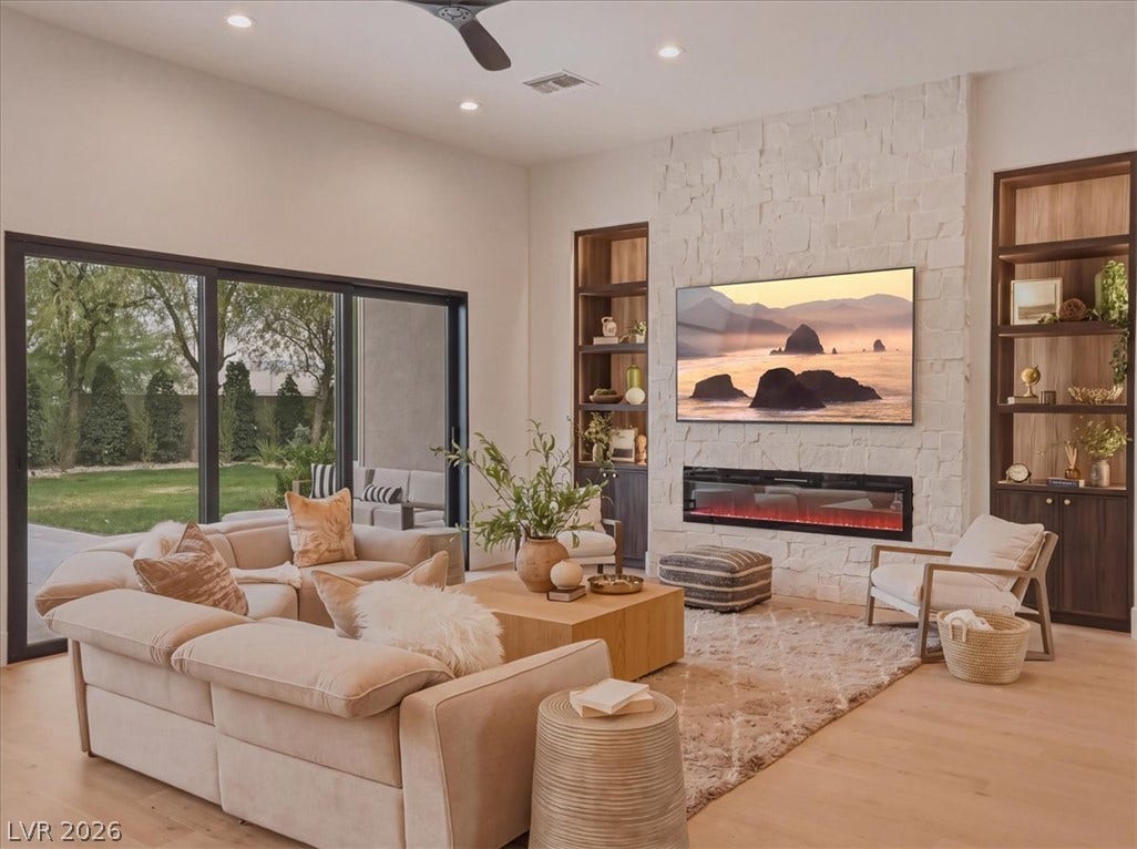 3 Isleworth Drive, Henderson, NV 89052 A spacious, naturally illuminated living area with light wood flooring and built-in shelving flanking a stone fireplace.