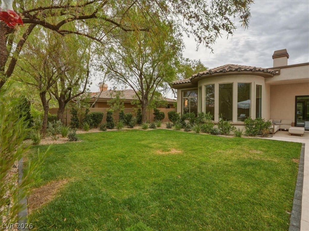 3 Isleworth Drive, Henderson, NV 89052 A well-maintained lawn stretches before a residence featuring a curved wall of large windows and a covered patio.