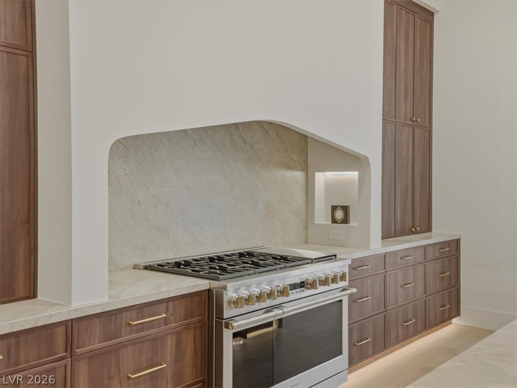 3 Isleworth Drive, Henderson, NV 89052 A well-appointed kitchen features a gas range set beneath an elegant arched hood, flanked by ample custom cabinetry.