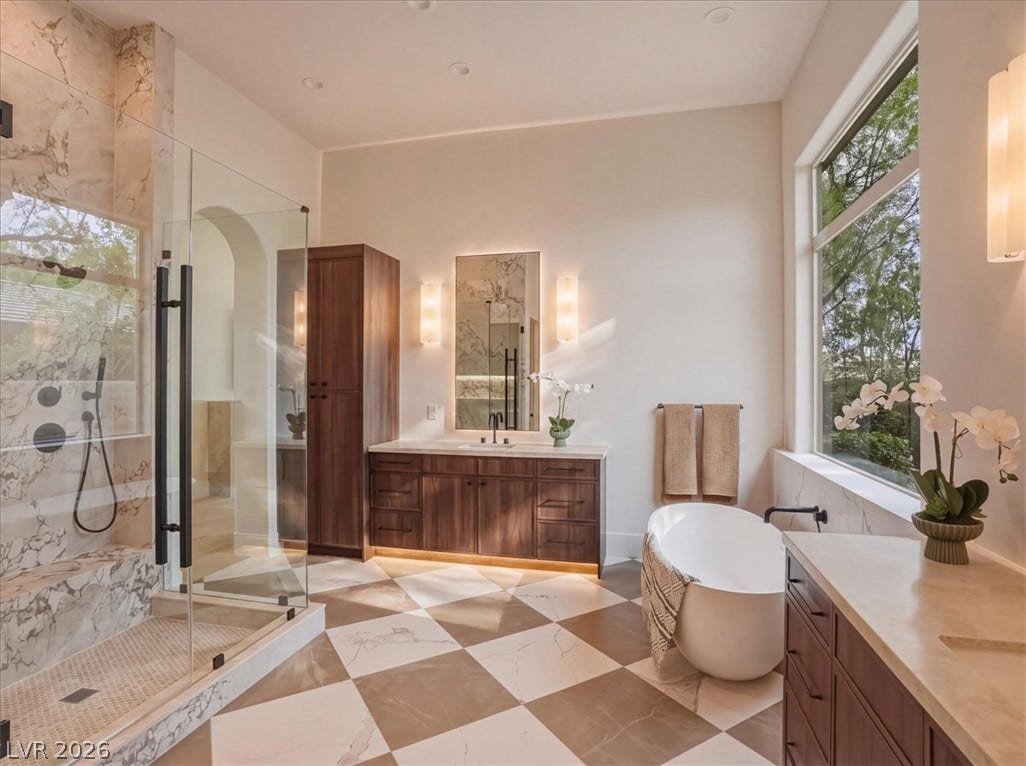 3 Isleworth Drive, Henderson, NV 89052 Luxurious bathing quarters with checkered marble flooring, a freestanding tub, and a spacious glass-enclosed shower.