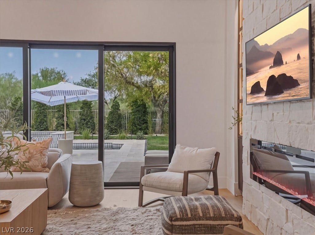 3 Isleworth Drive, Henderson, NV 89052 Floor-to-ceiling glass doors reveal a tranquil outdoor oasis with a tiled pool and mature trees.