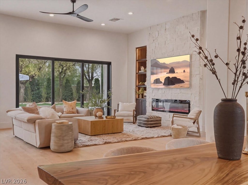 3 Isleworth Drive, Henderson, NV 89052 A spacious living area features wide glass doors, creating a fluid connection to the outdoors, complemented by an elegant stone fireplace.