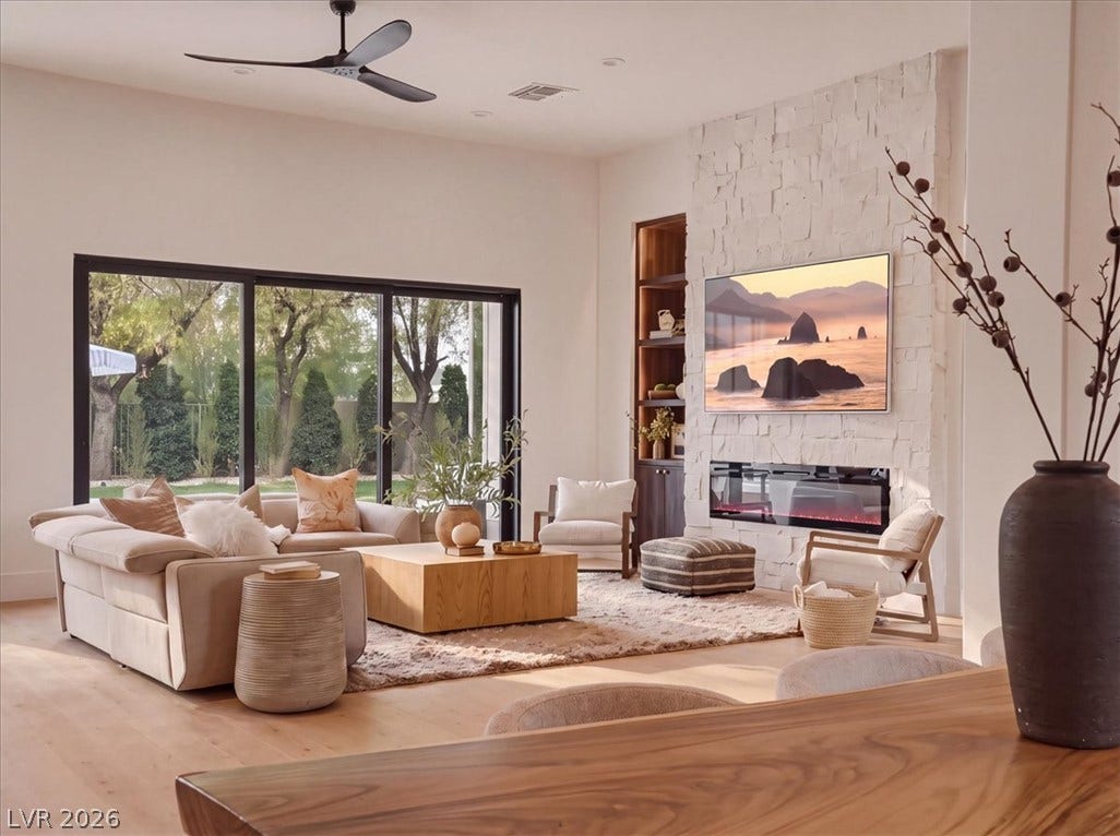 3 Isleworth Drive, Henderson, NV 89052 A spacious living area features wide glass doors, gleaming hardwood floors, and a modern fireplace integrated into a textured accent wall.