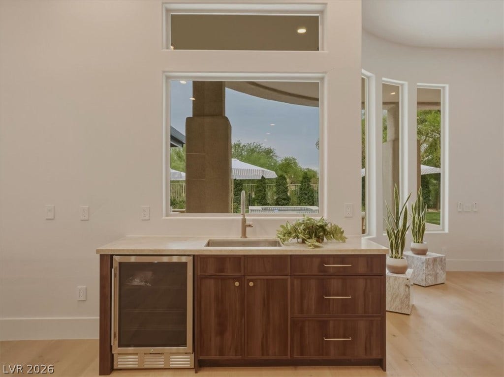 3 Isleworth Drive, Henderson, NV 89052 A refined wet bar with a wine cooler and light wood cabinetry is perfectly positioned beneath a broad window.