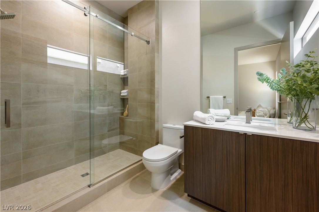 High-end finishes define this modern space featuring a glass-enclosed walk-in shower and stone countertops.