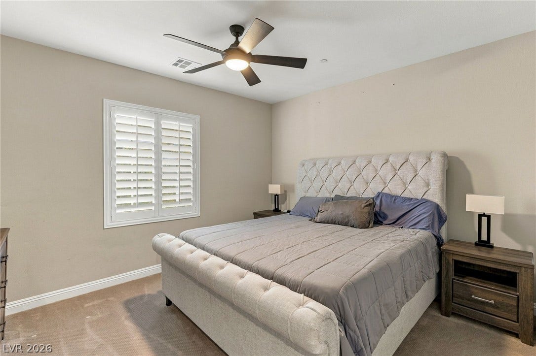 1372 Enchanted River Drive, Henderson, NV 89012 A spacious bedroom features soft carpeting, neutral walls, and a classic shuttered window.