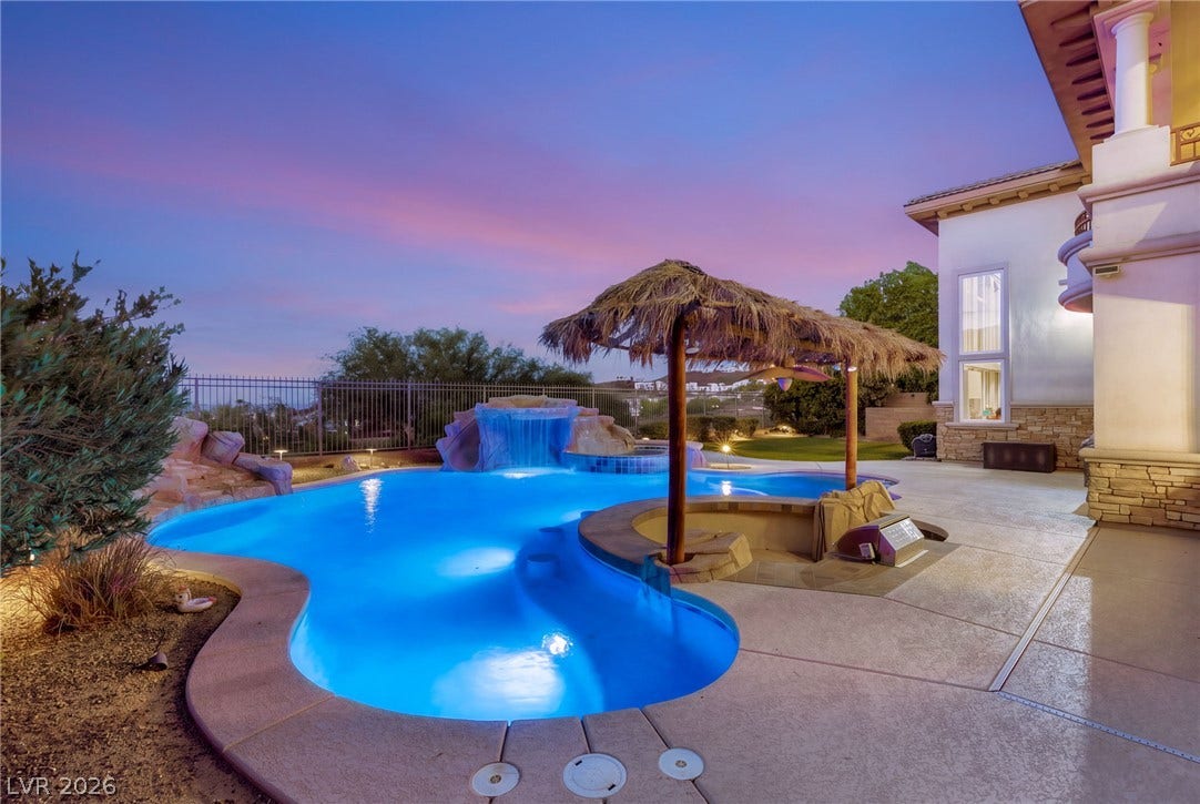 1372 Enchanted River Drive, Henderson, NV 89012 A custom rock waterfall pool highlights this backyard oasis under vibrant sunset skies.