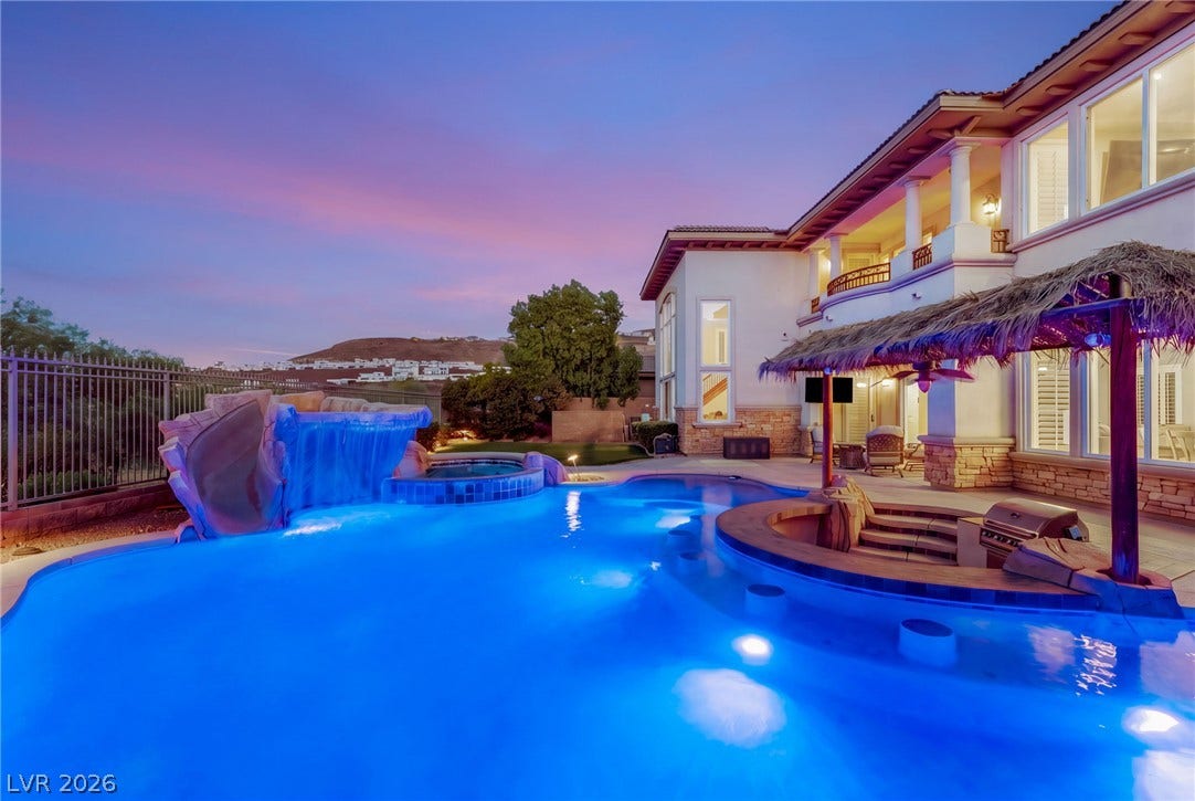 1372 Enchanted River Drive, Henderson, NV 89012 An illuminated resort-style swimming pool anchors this backyard oasis against a twilight sky.