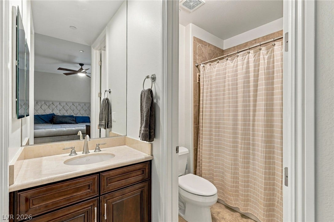 1372 Enchanted River Drive, Henderson, NV 89012 Crisp white walls frame a stone-topped vanity adjacent to a tiled tub and shower enclosure.
