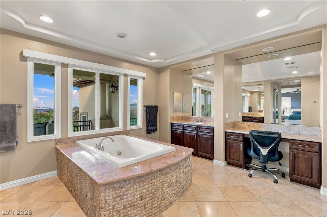 1372 Enchanted River Drive, Henderson, NV 89012 An inset soaking tub and expansive vanity mirrors define this well-appointed bathroom space.
