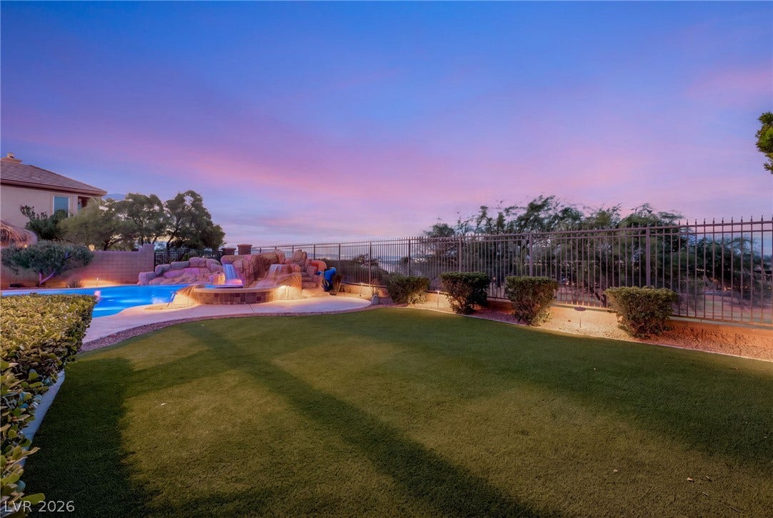 1372 Enchanted River Drive, Henderson, NV 89012 Manicured green lawn borders a resort-style swimming pool featuring custom rock waterfalls and protective fencing.